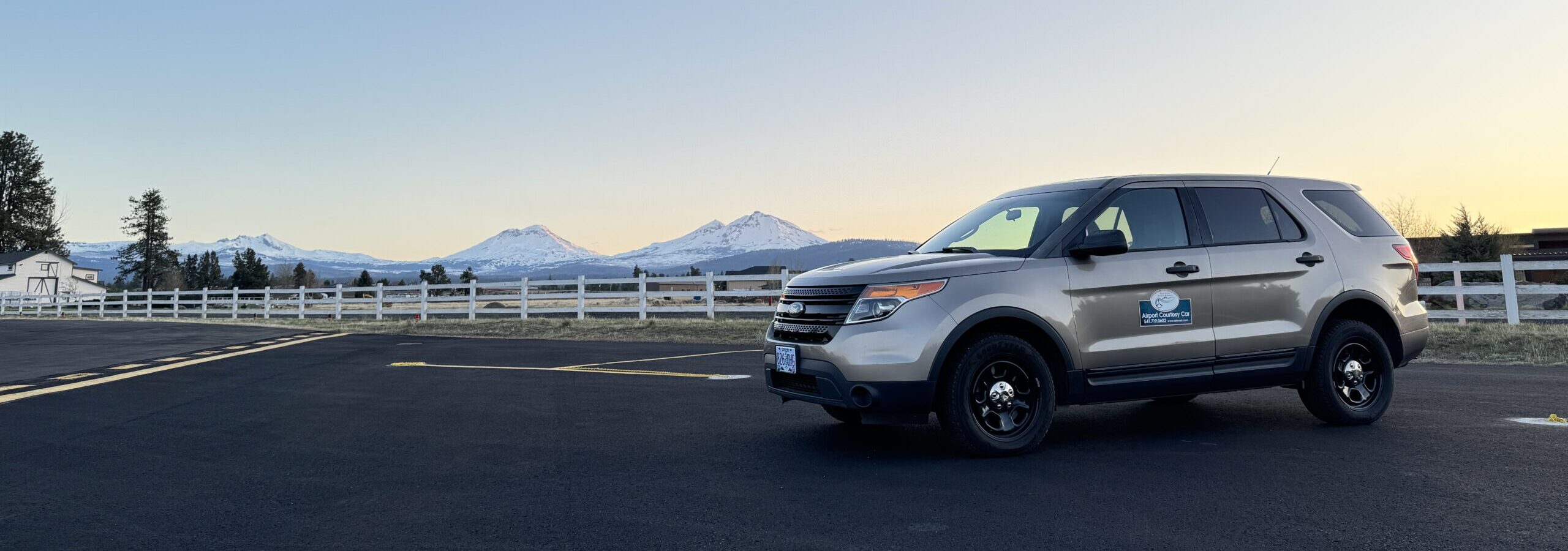 The Sisters Eagle Airport courtesy car parked on the ramp with the snow-capped Three Sisters peaks at sunset