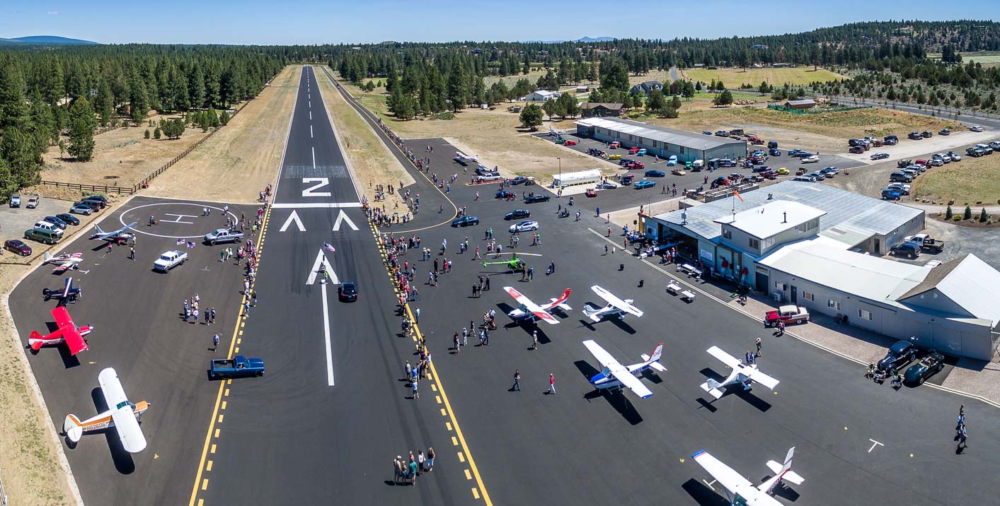 Aircraft and visitors along the flight line at a Sisters Eagle Airport fly-in, with the runway and Cascades beyond